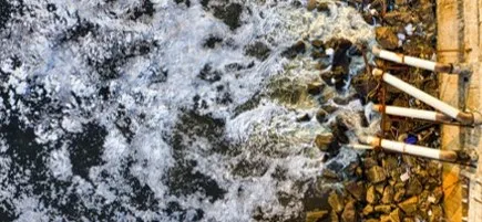 Foaming discharge entering a watercourse beside a debris-strewn bank